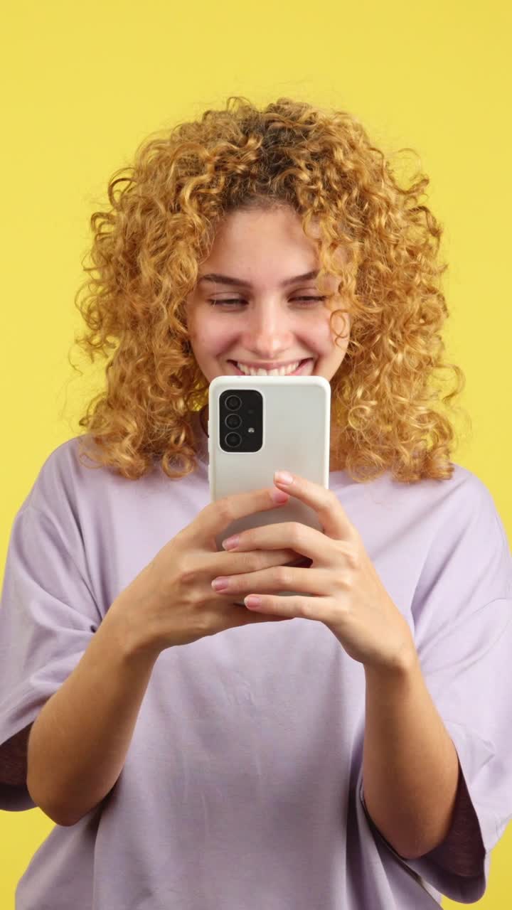 Smiling Woman Using a Smartphone on a Yellow Background