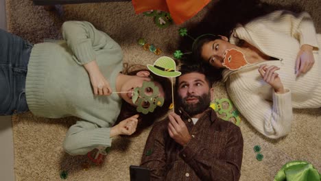 fotografía aérea de amigos disfrazados con novedades y accesorios irlandeses en casa posando para selfies celebrando en la fiesta del día de san patricio