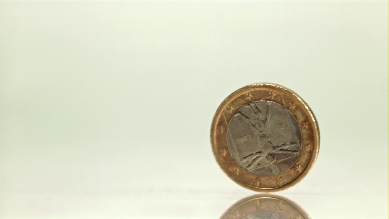 Primer plano de una moneda de euro girando y equilibrándose sobre una superficie reflectante