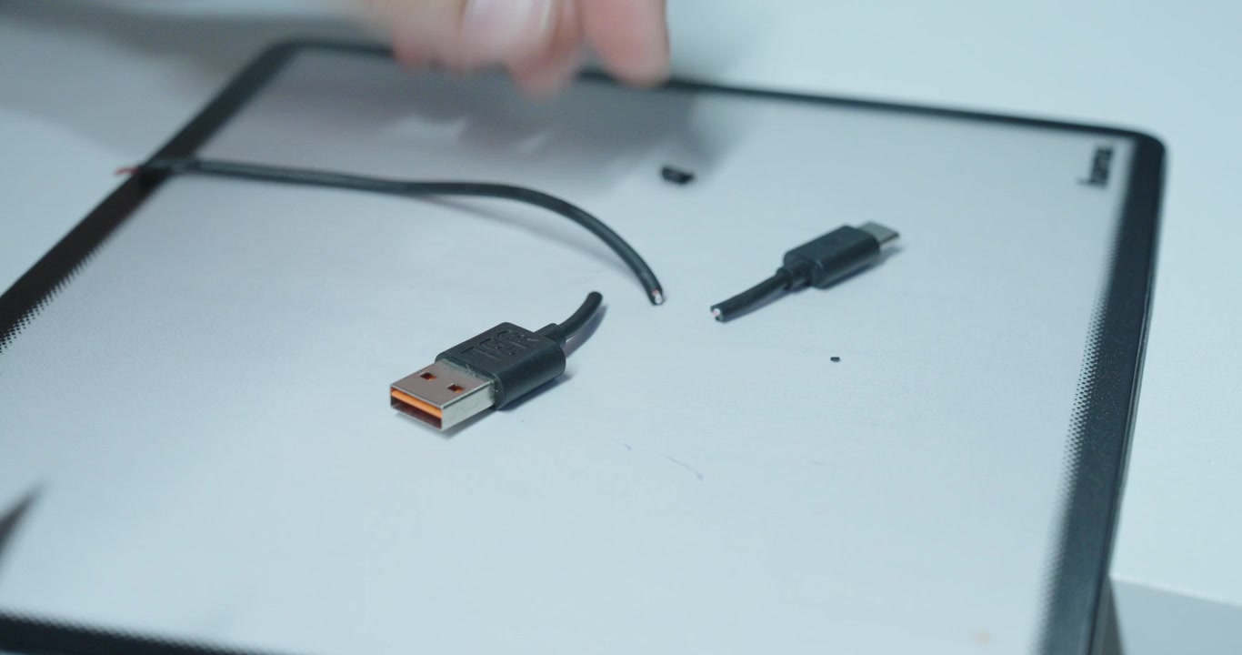 Person som klipper upp en USB-kabel för att modifiera den, visar risker med elektronisk reparation, skadade ledningar och osäker hantering