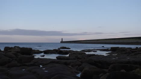 Gran-Angular-Fijo-Que-Establece-Un-Clip-De-Un-Largo-Muelle-Marino-Con-Un-Faro-Al-Final-Y-Rocas-Oscuras-Y-Pozas-De-Rocas-En-Primer-Plano