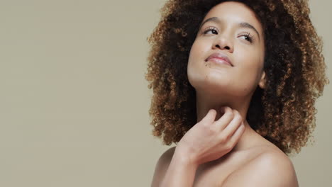 biracial woman with dark hair touching neck on beige background with copy space, slow motion