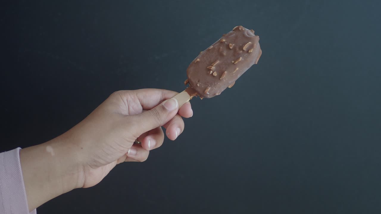 primer plano de una mano sosteniendo una barra de helado de almendra cubierta de chocolate