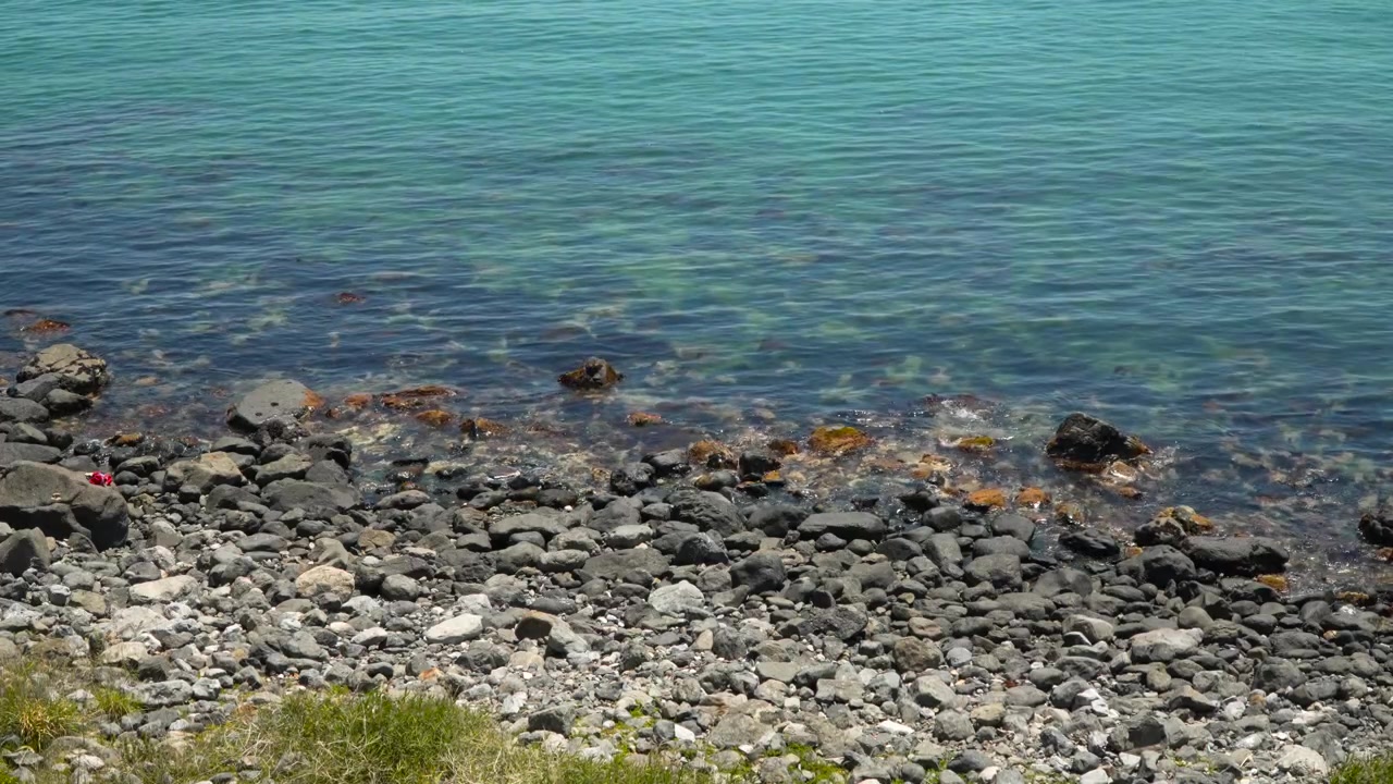 Klart turkist havvand, der skvulper over stenet rullestensstrand med brosten ved kystlinjen i Haeundae Blue Line Park i Busan, Sydkorea.