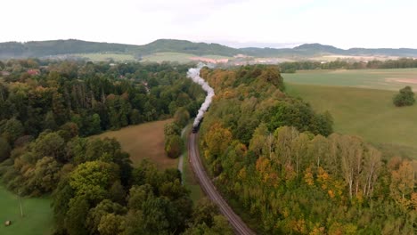 Aerial-view-of-an-autumn-landscape-with-a-passing-historical-steam-train-among-the-colorful-leaves-of-trees