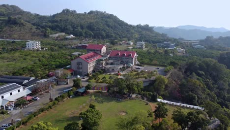 A-large-rural-estate-with-buildings-surrounded-by-greenery-in-daylight,-aerial-view