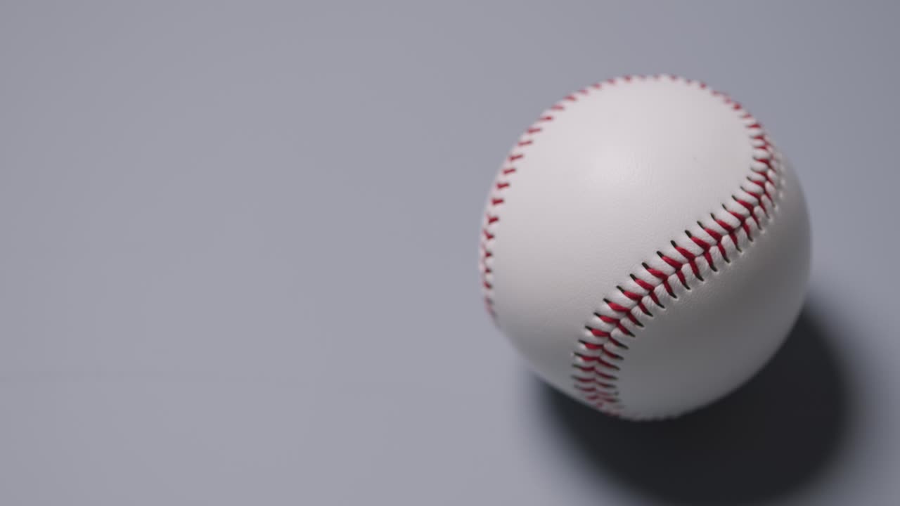 disparo de cerca de la mano recogiendo una pelota de béisbol contra un fondo gris