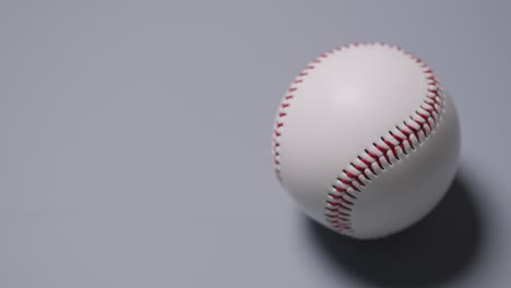 Close-Up-Shot-Of-Hand-Picking-Up-Baseball-Ball-Against-Grey-Background