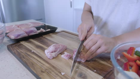 Side-on-close-up-shot-of-woman-in-kitchen-preparing-chicken-and-vegetables-for-asian-stir-fry