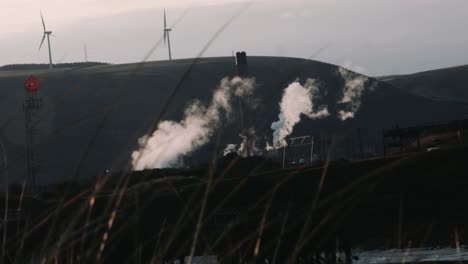 cinematic slow motion of industrial steelworks plant with wind turbines in background