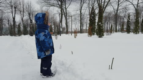 caucasian toddler in blue clothes stands in winter. side view. baby boy points at something in front of him.