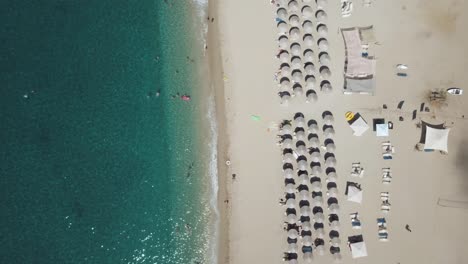 Flying-above-an-organized-beach-with-turquoise-blue-water-and-a-white-sand-beach,-top-view,-aerial-with-the-ocean-on-the-left