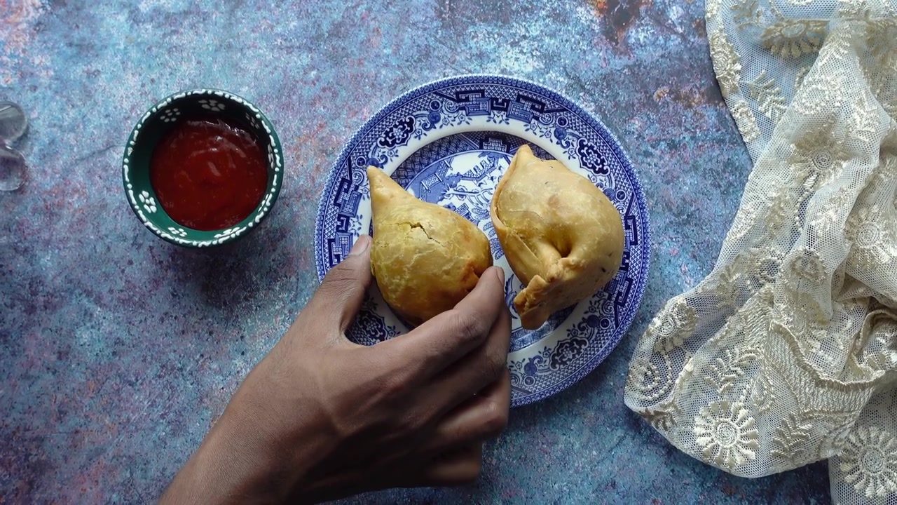 Mano che prende un samosa croccante da un piatto decorativo