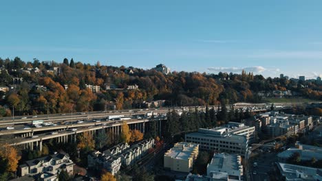 El-Dron-Asciende-Por-Encima-De-Los-Edificios-De-Apartamentos-Para-Revelar-Una-Carretera-Muy-Transitada-Con-Follaje-De-Otoño-Que-Bordea-La-Carretera.