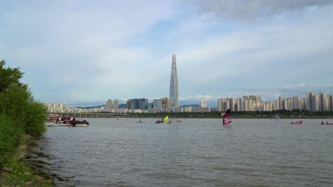 Windsurf,-Kayak-Y-Remo-En-El-Río-Han-Con-El-Horizonte-De-La-Ciudad-De-Seúl,-Corea-Del-Sur-En-El-Fondo