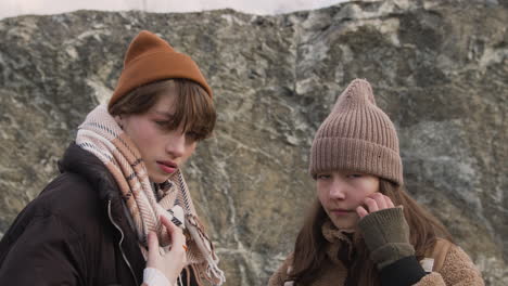 vista ravvicinata di due ragazze adolescenti in abiti invernali che si pongono alla macchina fotografica sulla montagna in una giornata ventosa