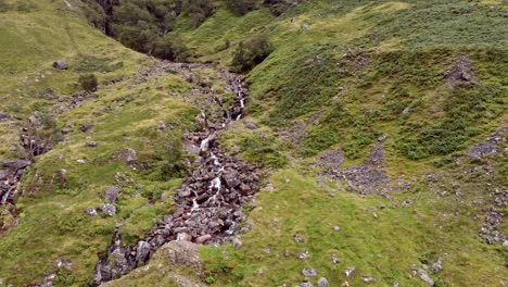 aerial view, slowly pulling back from a close up of a steep rocky stream on the lush, green valley hillside of glen coe, scotland