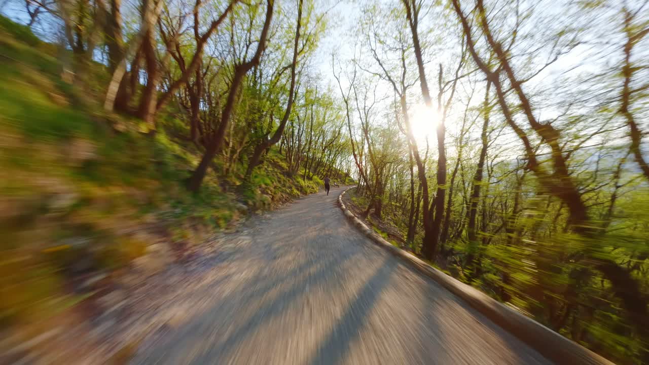 Young man running on a forest path with FPV drone perspective, trees and sunlight