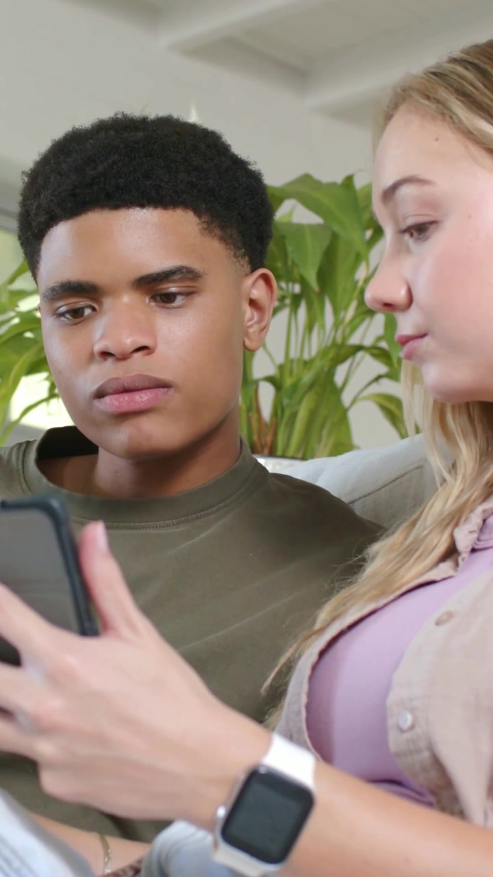 Vertical video: Woman turning phone toward man, couple leaning on couch at home, studying screen