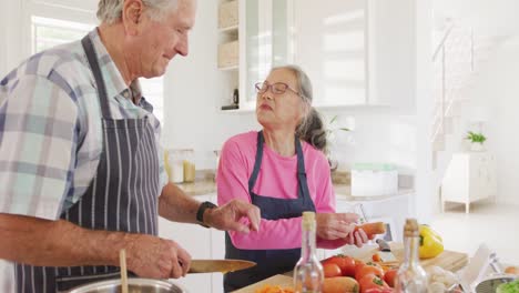 feliz pareja de ancianos diversos usando delantales y cocinando en la cocina