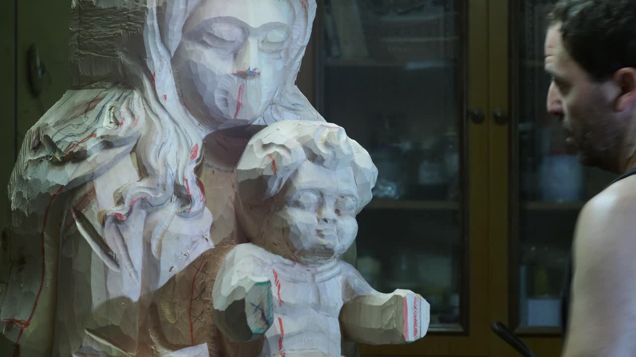 Professional sculptor carving delicate wooden statue with traditional chisel, showcasing meticulous craftsmanship inside well-organized workshop studio