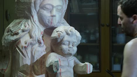 professional sculptor carving delicate wooden statue with traditional chisel, showcasing meticulous craftsmanship inside well-organized workshop studio