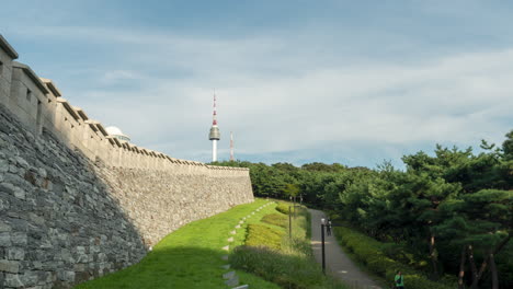 n seoul tower or namsan tower and seoul city wall hanyangdoseong, timelapse of korean people and tourists walking on footway in a mountain green park - zoom in motion