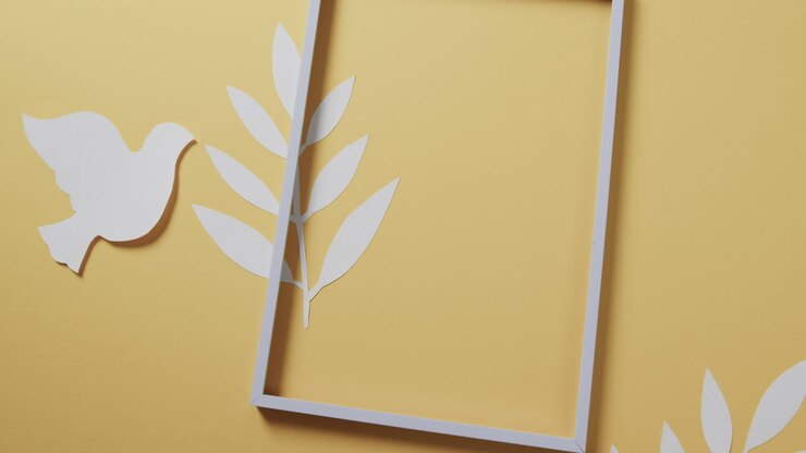 Close up of white dove with frame and leaves and copy space on yellow background
