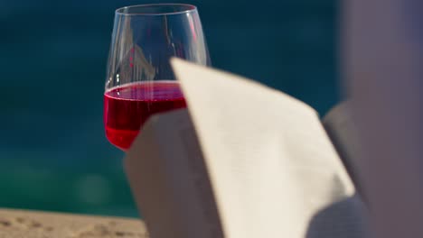 toma de primer plano de una copa de vino con una chica volviendo las páginas de un libro y el viento soplando por el océano en sicilia, italia (sicilia, italia)