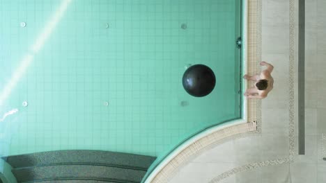 Overhead-view-of-woman-jumping-onto-exercise-ball-in-pool-and-failing-to-hold-on