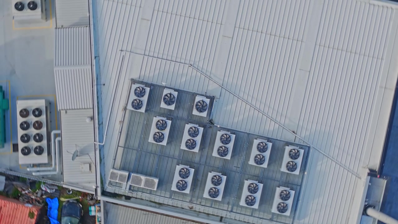 Drone footage captures a data center rooftop lined with industrial HVAC units and metallic panels, featuring clear geometric lines, even lighting, and crisp overhead composition for technology themes.