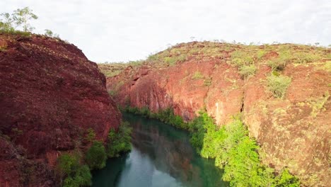 drone volando directamente a través de un cañón con grandes paredes de roca roja a cada lado y un río tranquilo debajo