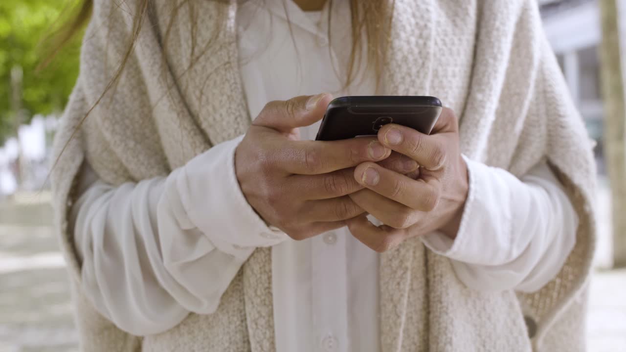 una foto recortada de una mujer con abrigo blanco sosteniendo un teléfono inteligente.