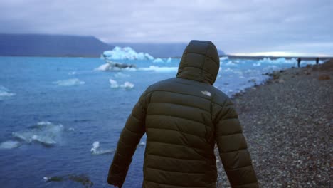 man in winter coat walking by the jokulsarlon glacial lagoon in iceland