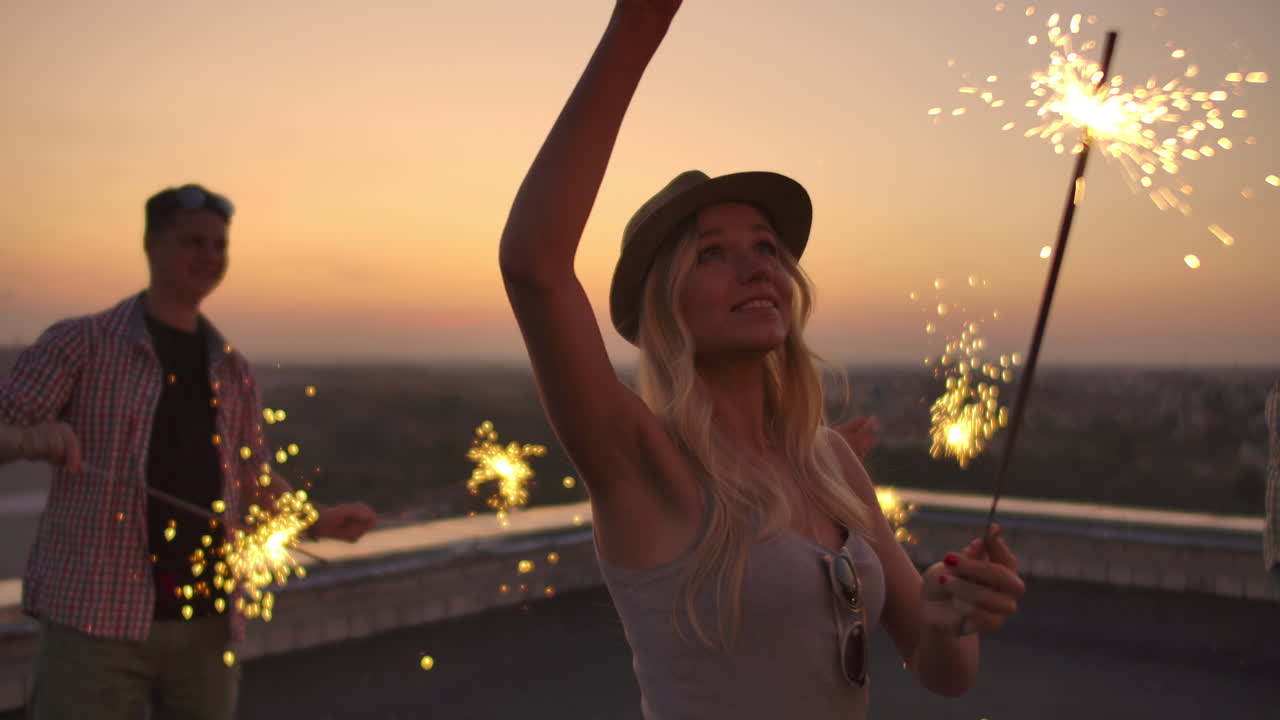 Girl on the roof moves and dance with her friends on a summer evening with big bengal light. It's a pleasure sunset before night. Their hair blows beautifully in the wind.