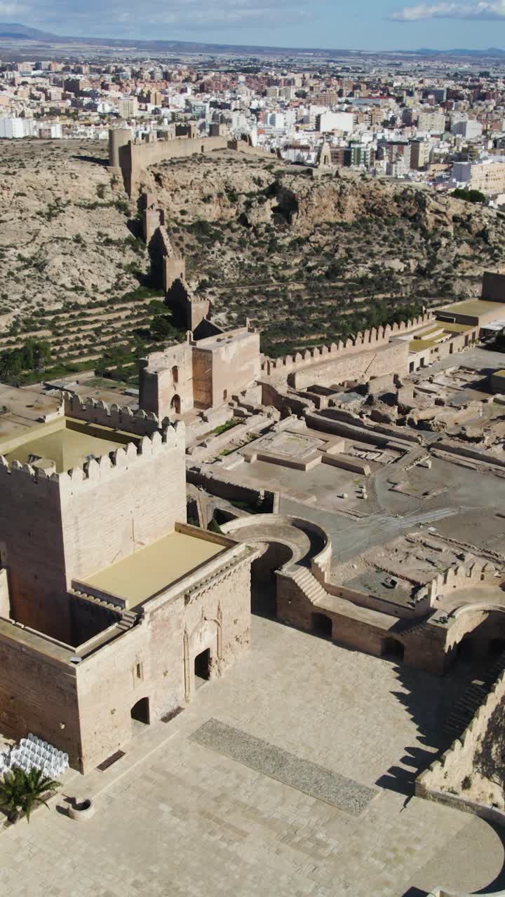 Ripresa aerea verticale con drone orbitante intorno alla storica Alcazaba di Almería, che mostra la fortezza e il paesaggio andaluso circostante