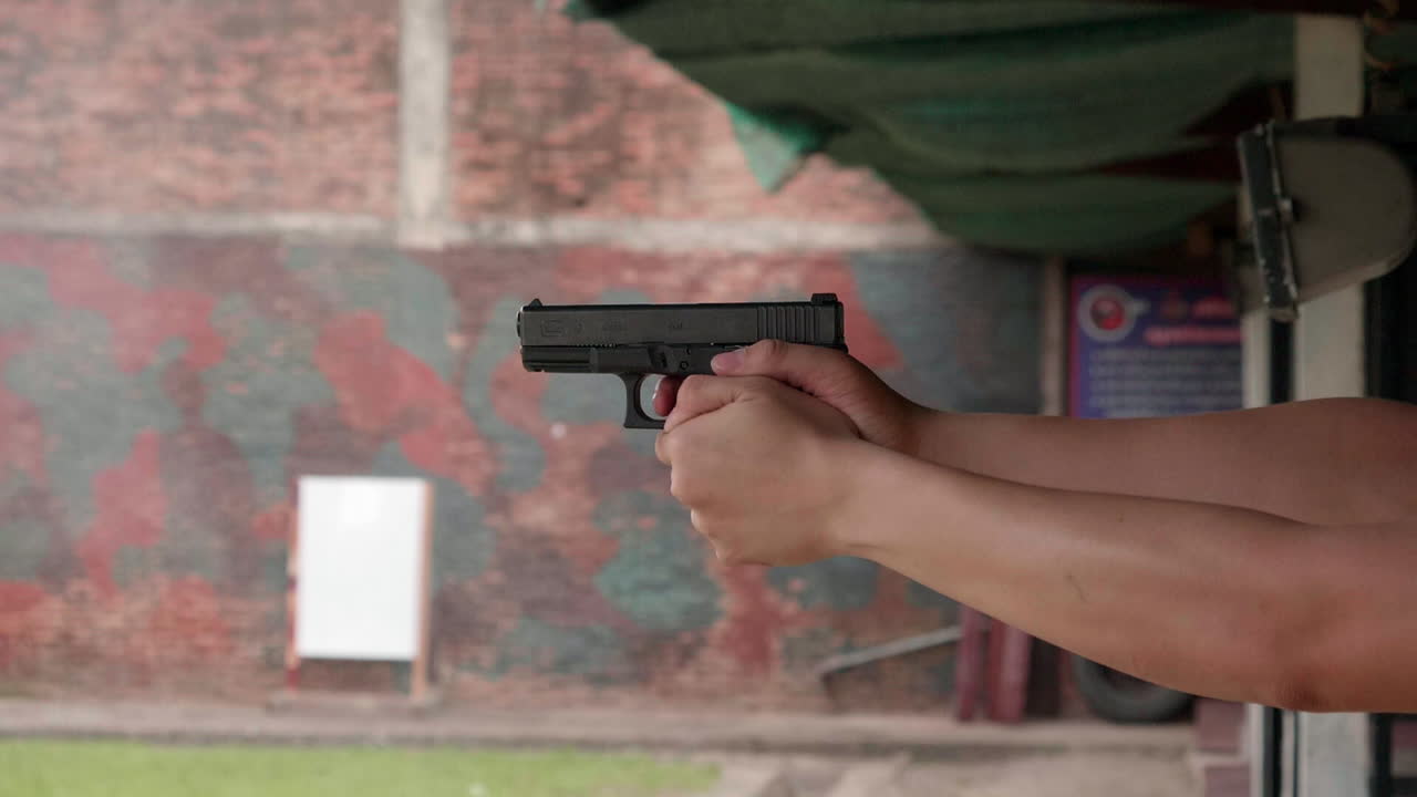 남자 손의 사격장에서 총을 발사하는 슬로우 모션 장면은 총을 단단히 잡고 방아쇠를 당깁니다