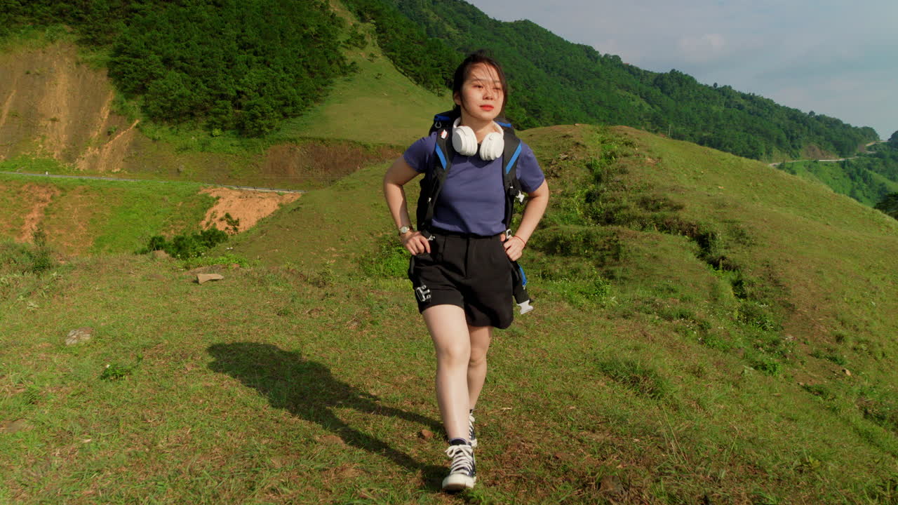 young asiatic female solo traveller walking alone with backpack on mountains trekking path with headphone in slow motion celebrating life