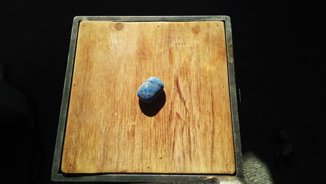 medium shot of a hand entering frame and placing a semi precious stone on wooden display