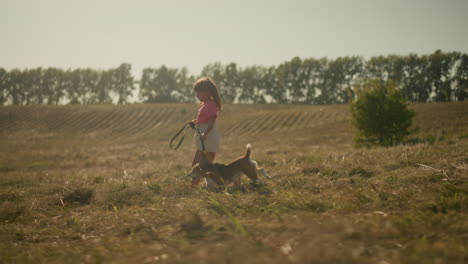 side view of young girl joyfully running with her dog while holding leash in open farmland, scene shows carefree childhood, companionship with pet, and outdoor exploration