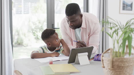 african american man helps a boy with homework at home using a tablet