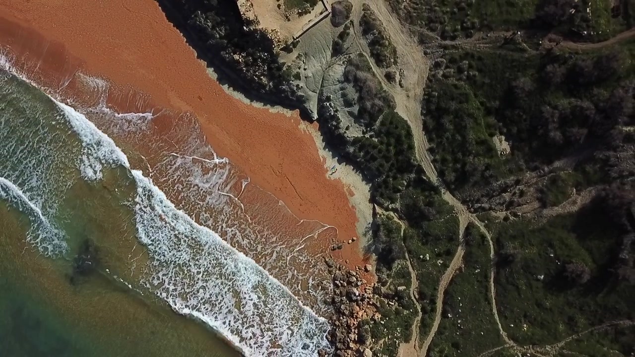 Veduta aerea dall'alto di una spiaggia sabbiosa unica color oro-arancio sull'isola di Gozo. Onde armoniose che si infrangono sulla sabbia, donando una rilassante sensazione estiva