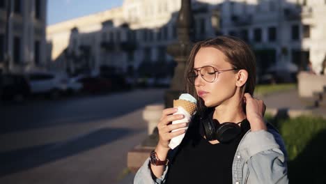 Mujer-Joven-En-Camisa-Naranja-Disfrutando-De-Helado-De-Vainilla-Suave-En-Cono-De-Gofre-Al-Aire-Libre-En-Cámara-Lenta