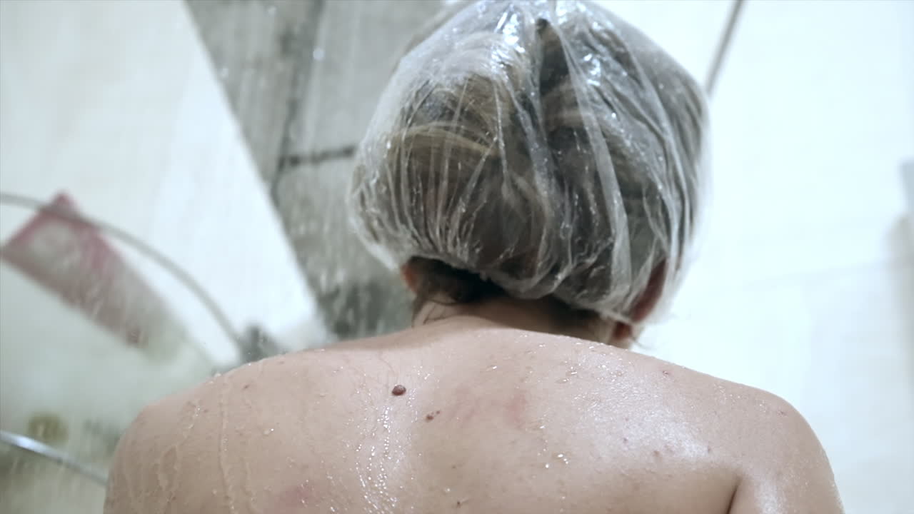 Close up of a woman showering with a shower cap on her head