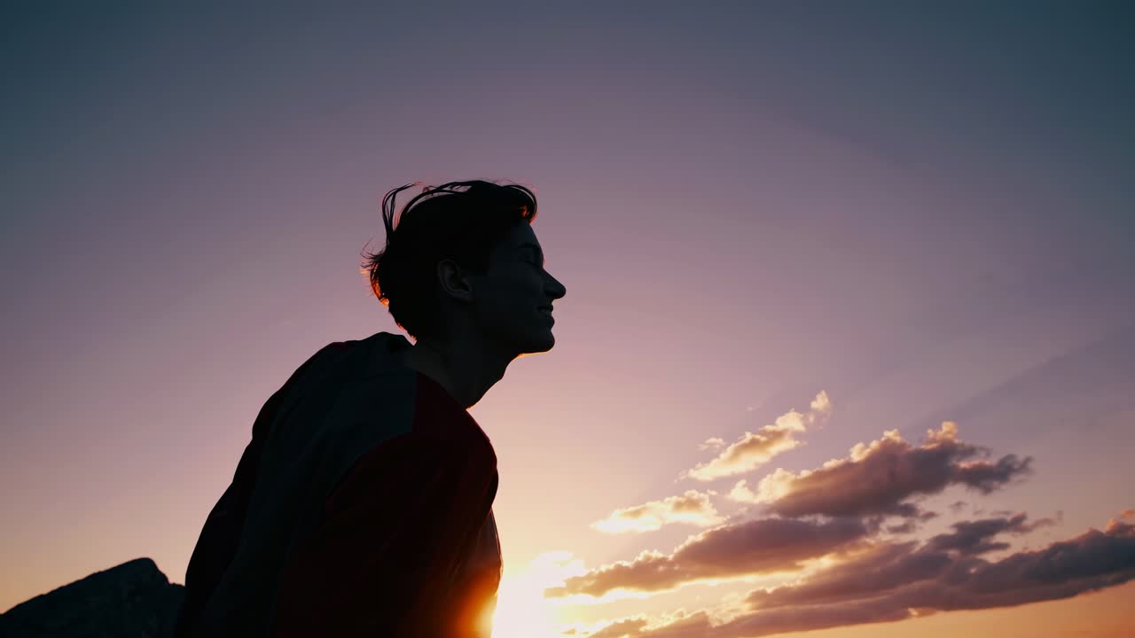 Silhouette of a person against a vibrant sunset sky, captured from a low angle