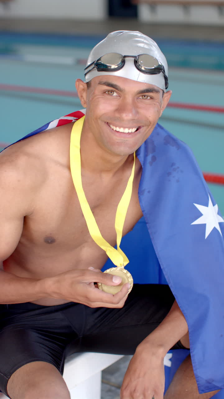 Vertical video: Strong and fit swimmer holding gold medal and smiling, wearing swim cap and goggles