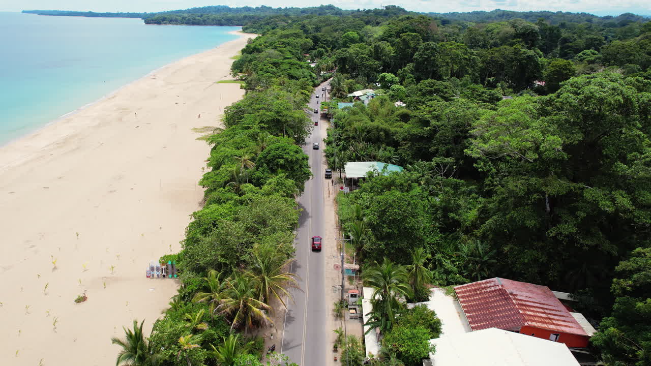 A cinematic overhead shot descending over road of tourists driving down the beach Playa Cocles revealing the popular tourist destination Puerto Viejo on the Caribbean coast of Costa Rica.