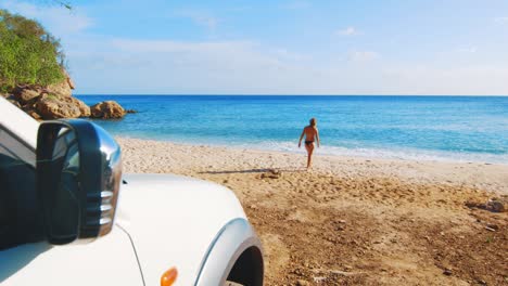 coche en primer plano con una chica caminando en bikini hacia la playa en el fondo