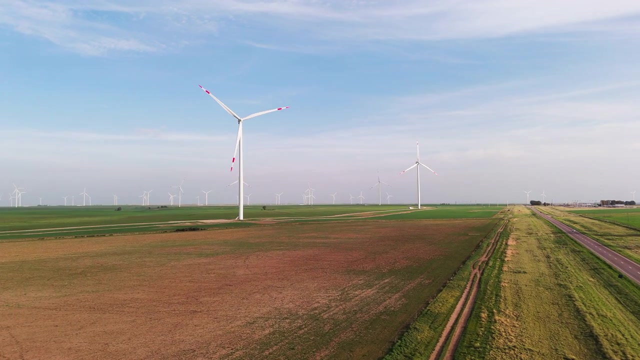 Aerial windmills and green, brown fields on a cloudy day, passing a street with cars, slow motion, copy space