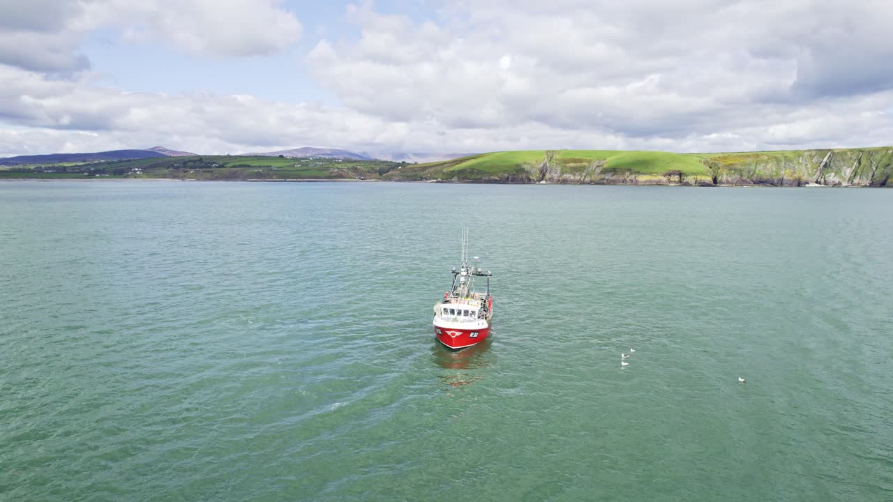 barco de pesca en el trabajo frente a la costa de waterford irlanda con acantilados marinos y montañas en el fondo en un vibrante día de primavera